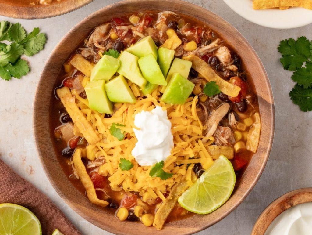 An overhead shot of chicken tortilla soup with cheese, avocado and a lime wedge.