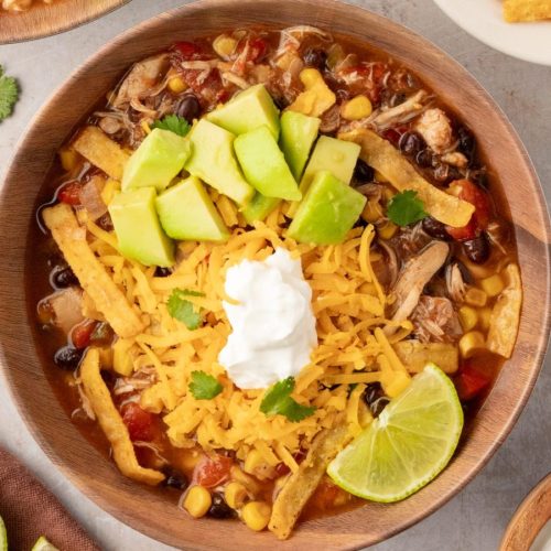 An overhead shot of chicken tortilla soup with cheese, avocado and a lime wedge.