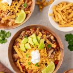 Overhead shot of 2 bowls of slow cooker chicken tortilla soup topped with avocado, cheese and sour cream with a lime wedge.