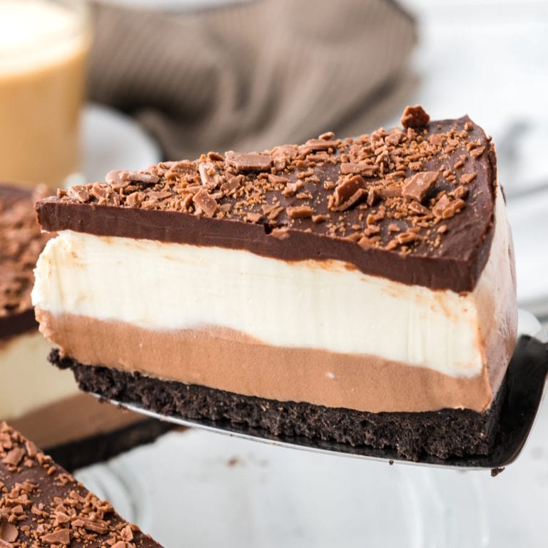 A closeup of Layered Chocolate Cheesecake being served from a glass server.