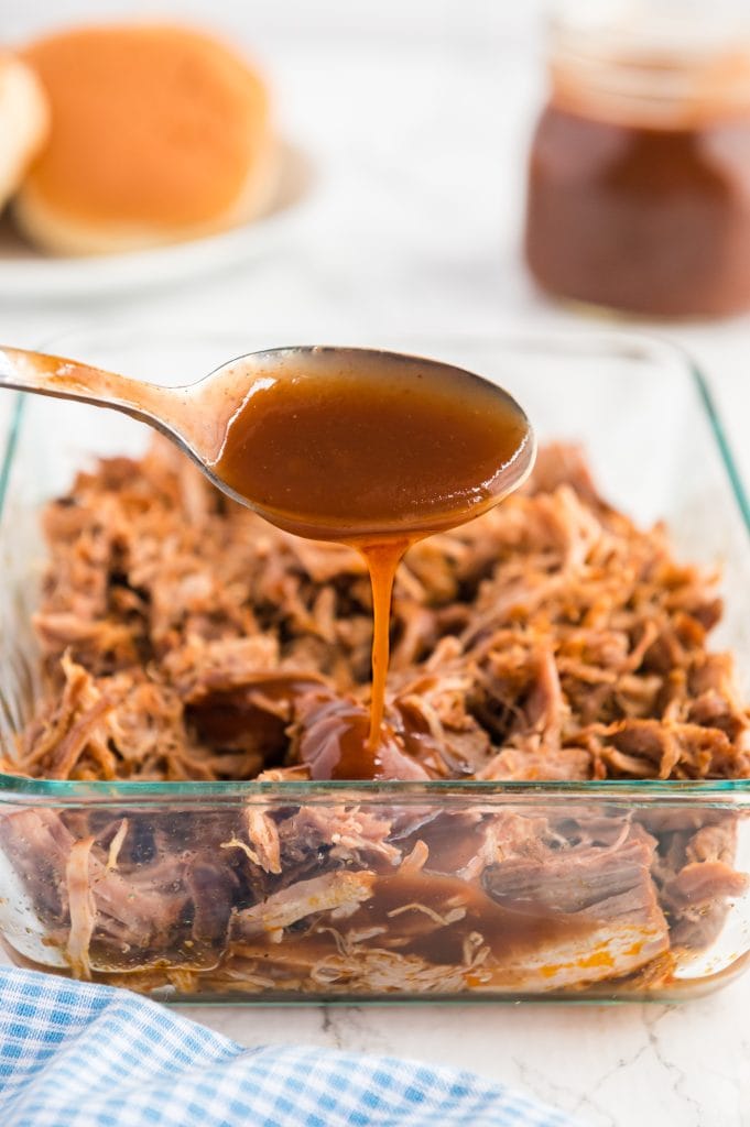 A spoonfull of bbq sauce being poured ontop on pulled pork