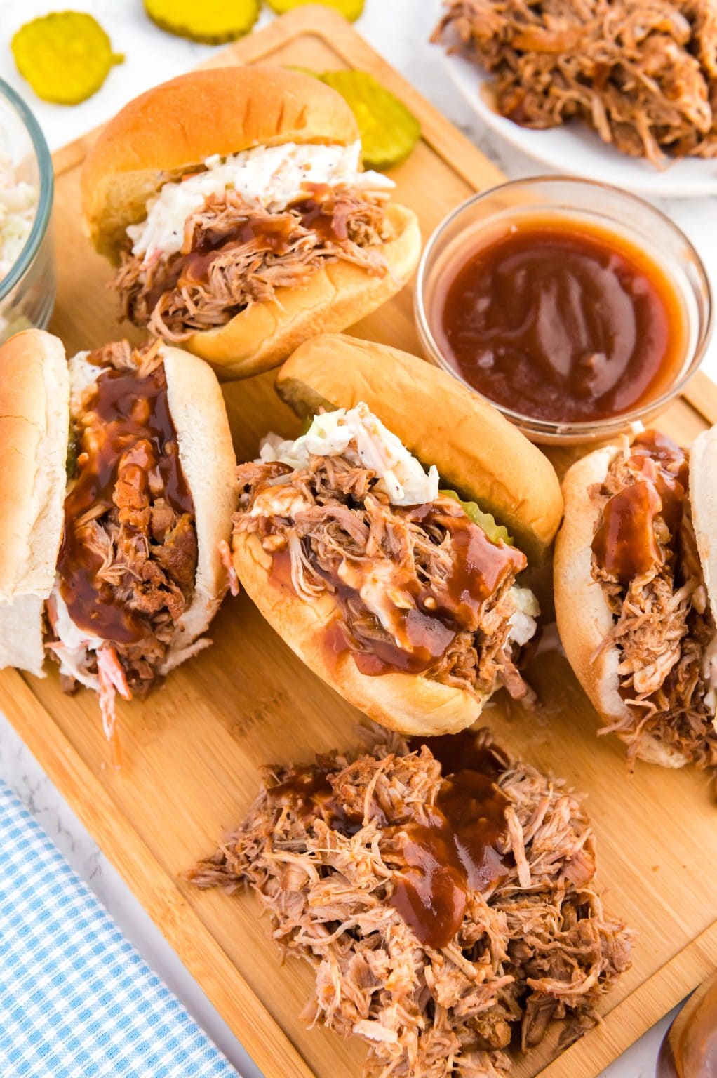 lots of pulled pork sandwiches on a wooden board with lots of bbq sauce