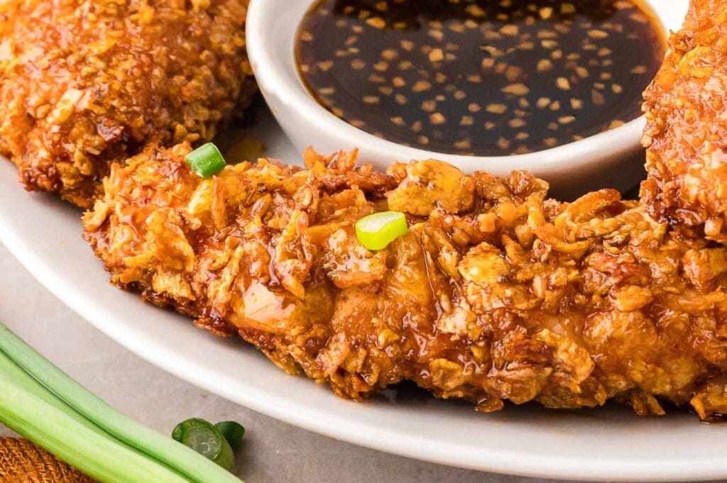 Air fryer chicken teders on a white plate with honey garlic sauce in a bowl.