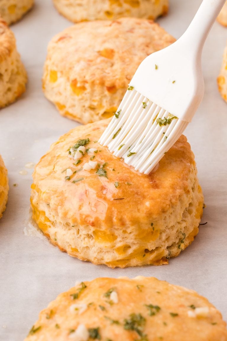 A white brush applying garlic butter to the cheddar garlic biscuits.