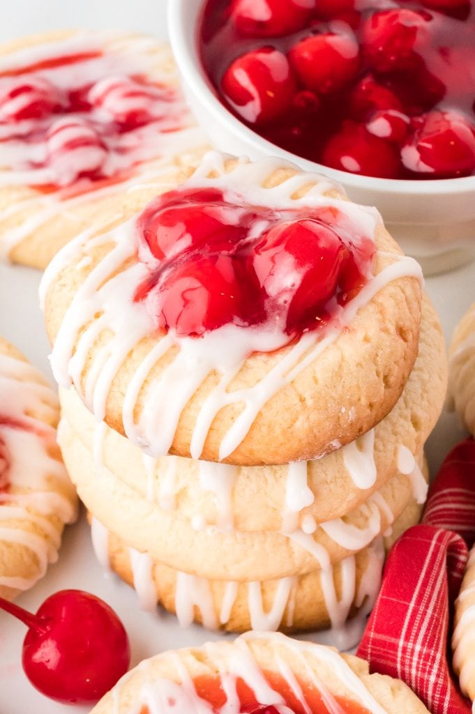 A stack of cherry pie cookies with icing and cherry topping.