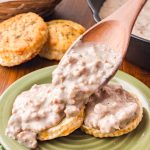 Southern sausage gravy being spooned over biscuits.