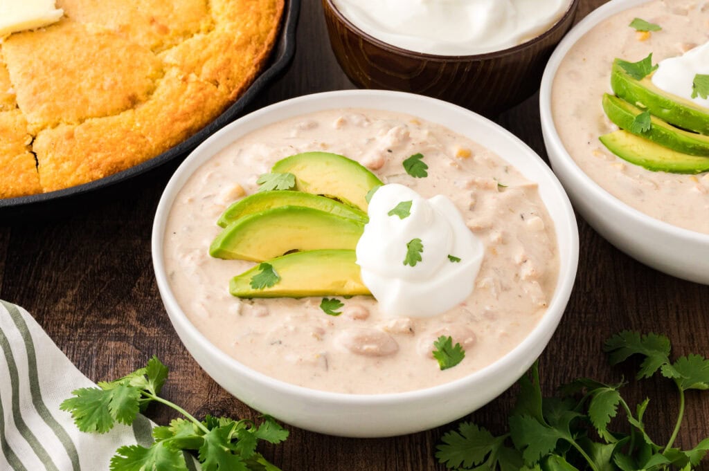 Up close shot of a bowl of white chicken Chili with cheese, avocado and sour cream by Tessies Table