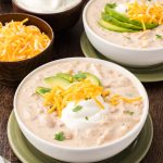 White Chicken Chili in bowls with avocado, cheese and sour cream.