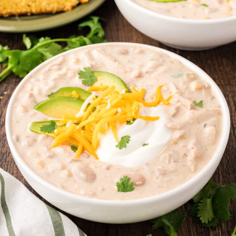 Up close shot of a bowl of white chicken Chili with cheese, avocado and sour cream.