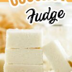 A close-up of thick white coconut fudge squares stacked with shredded coconut on top.