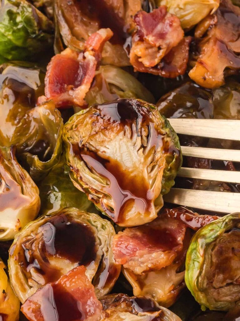 A fork with a cooked brussel sprouts and bacon and balsamic glaze.