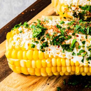 A close up of Mexican Elotes lying on a wooden board.