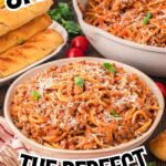 One pot spaghetti served in a bowl with grated cheese on top, with breadsticks and a serving dish of spaghetti in the background on a wooden table.