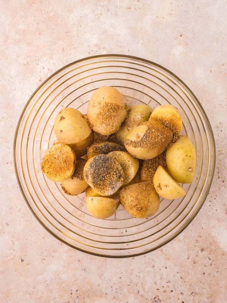 Bowl with raw potatoes , salt , pepper, cajun seasoning and oil.