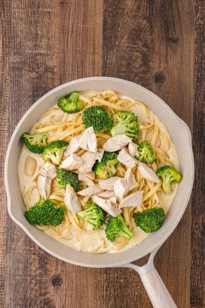 Cooked chicken and broccoli in a pan with pasta and cream alfredo sauce.