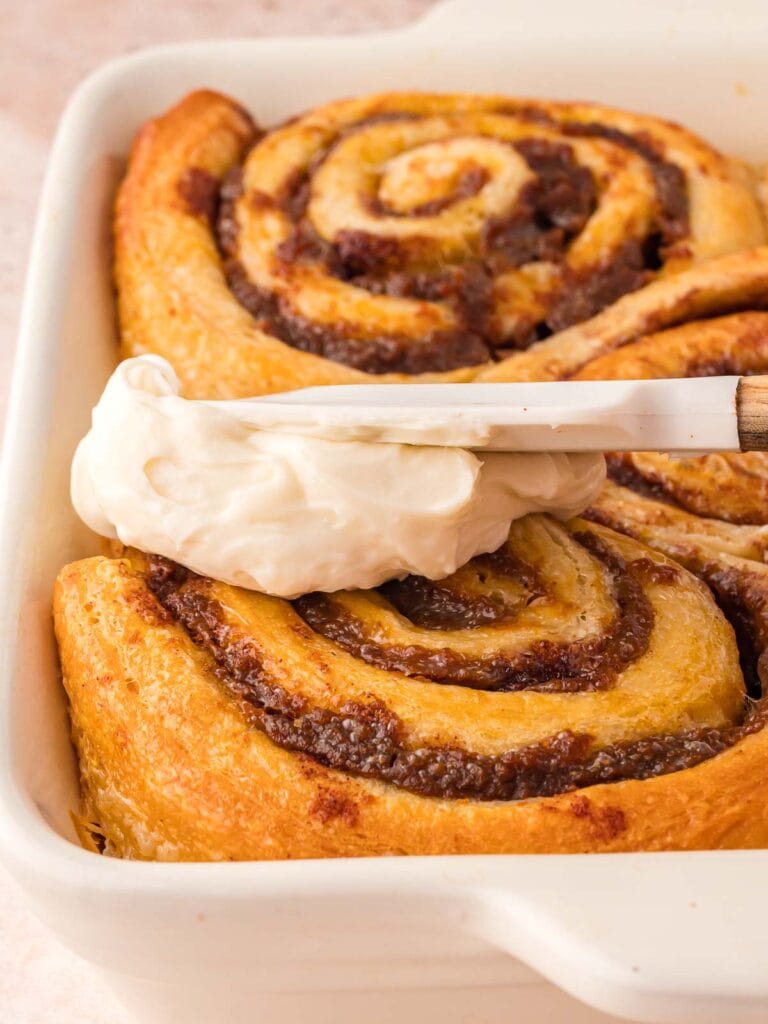 Maple Cream Cheese Frosting being spread over Pumpkin Cinnamon Rolls.