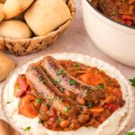 a plate of mashed potatoes with the sausage casserole poured ontop with a basket of bread.