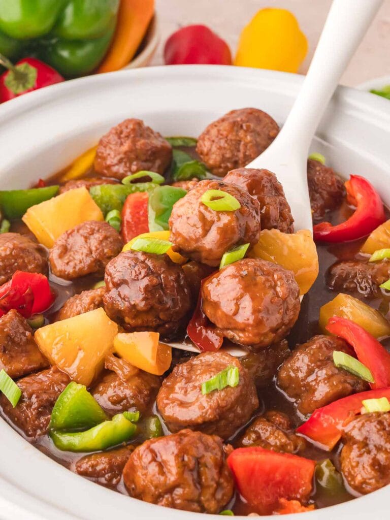 Spoonful of fully cooked sweet and sour meatballs in a slow cooker.