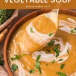 Spoonful of creamy homemade vegetable soup lifted from a wooden bowl garnished with parsley by Tessie's Table.