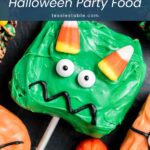 Close-up of a green monster treat with candy corn horns and candy eyes next to a candy pumpkin by Tessie's Table.