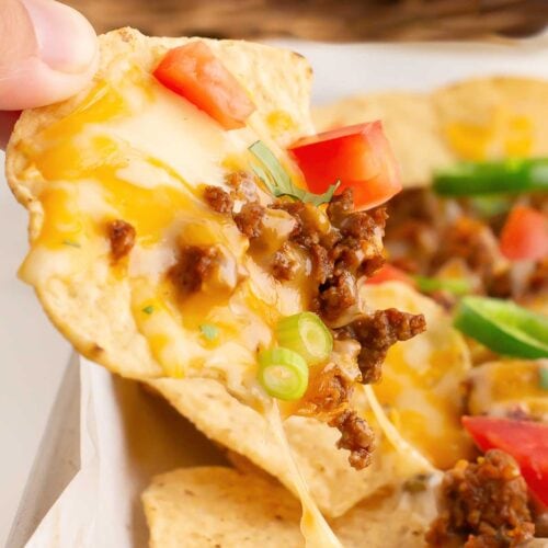 A hand lifting up Beef Nachos with cheese, beef and toppings.