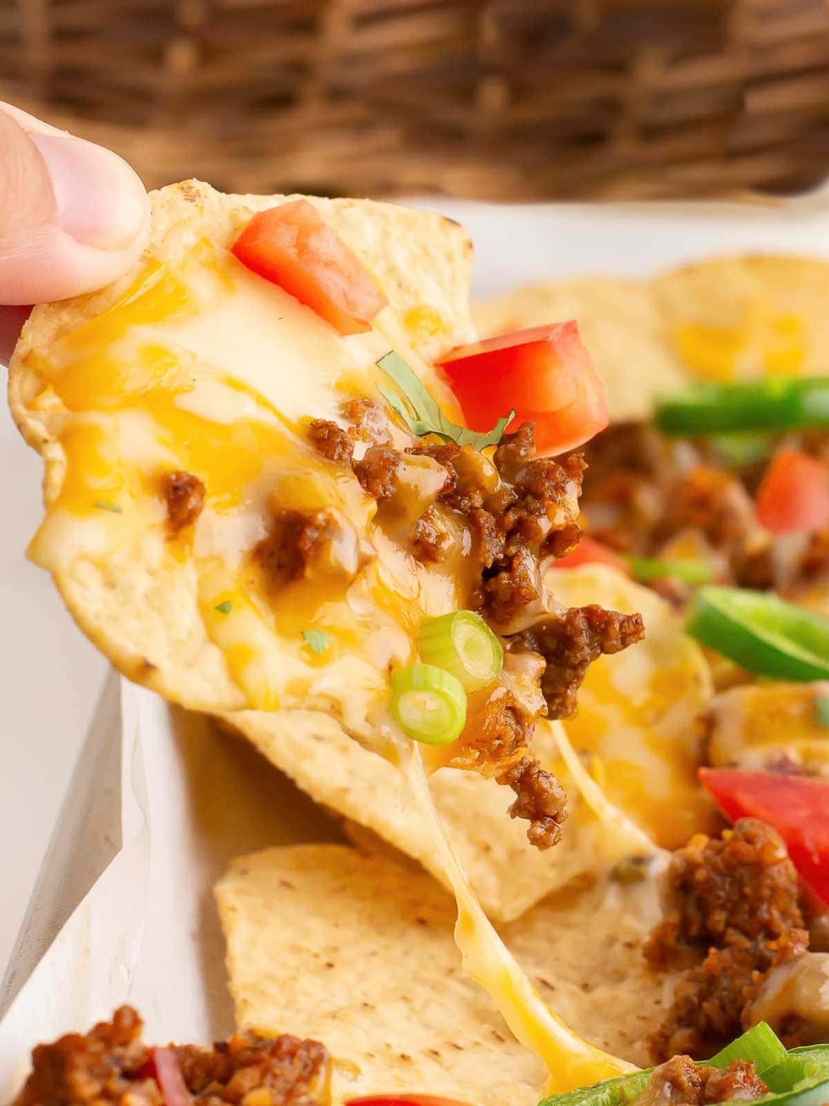 A hand lifting up Beef Nachos with cheese, beef and toppings.