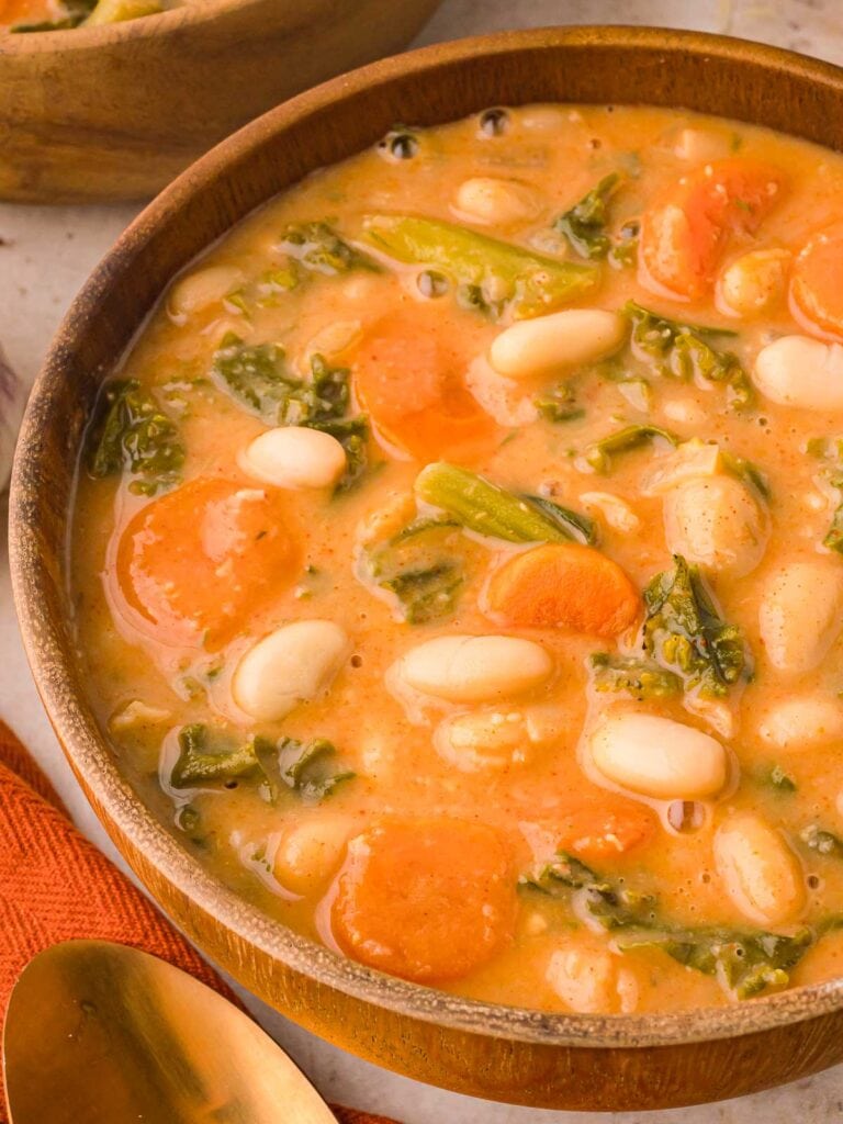 Up close of the kale and white bean soup in a wooden bowl.