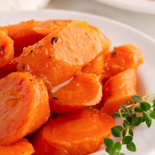 Up close of Honey Glazed Carrots. on a white plate with fresh thyme.