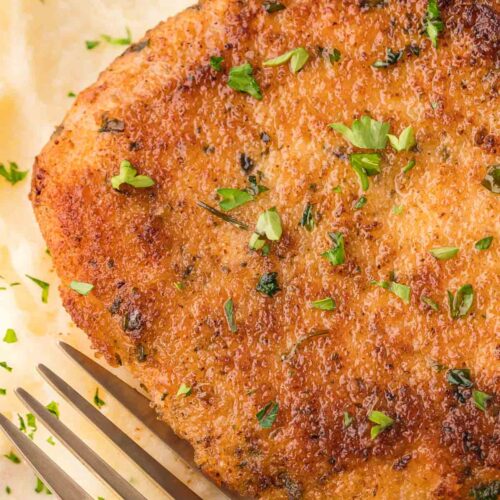 Up close Parmesan Crusted Pork Chop on a bed of mashed potatoes with a fork.