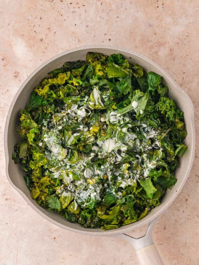 Heavy cream added to the kale in the pan.