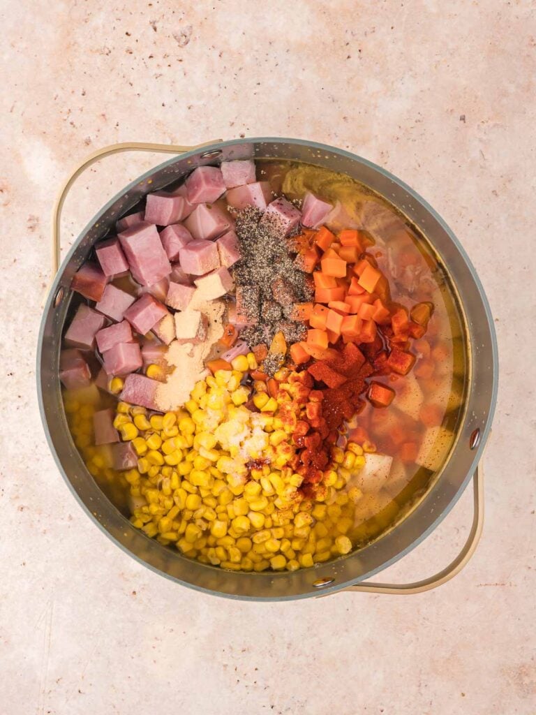 Potatoes, ham, carrots, sweet corn and chicken broth in a pot.