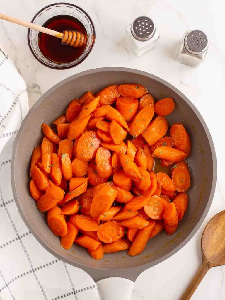 Carrots tossed in the honey butter in a skillet.