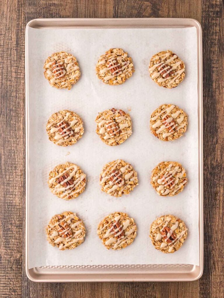 Maple pecan cookies with a pecan in the center of each cookie and maple glaze drizzled over the top.