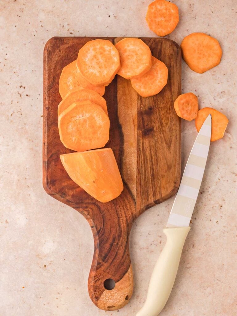 Wooden chopping board with sliced sweet potatoes.