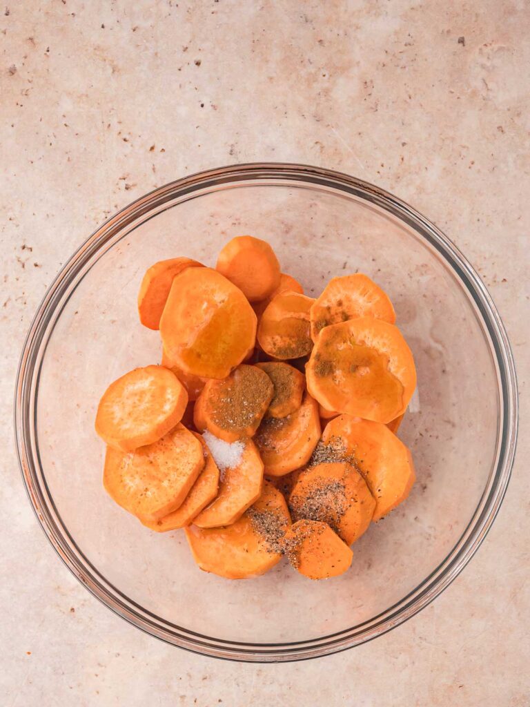 A bowl with sweet potatoes, oil, cinnamon, maple syrup, salt and pepper in it.