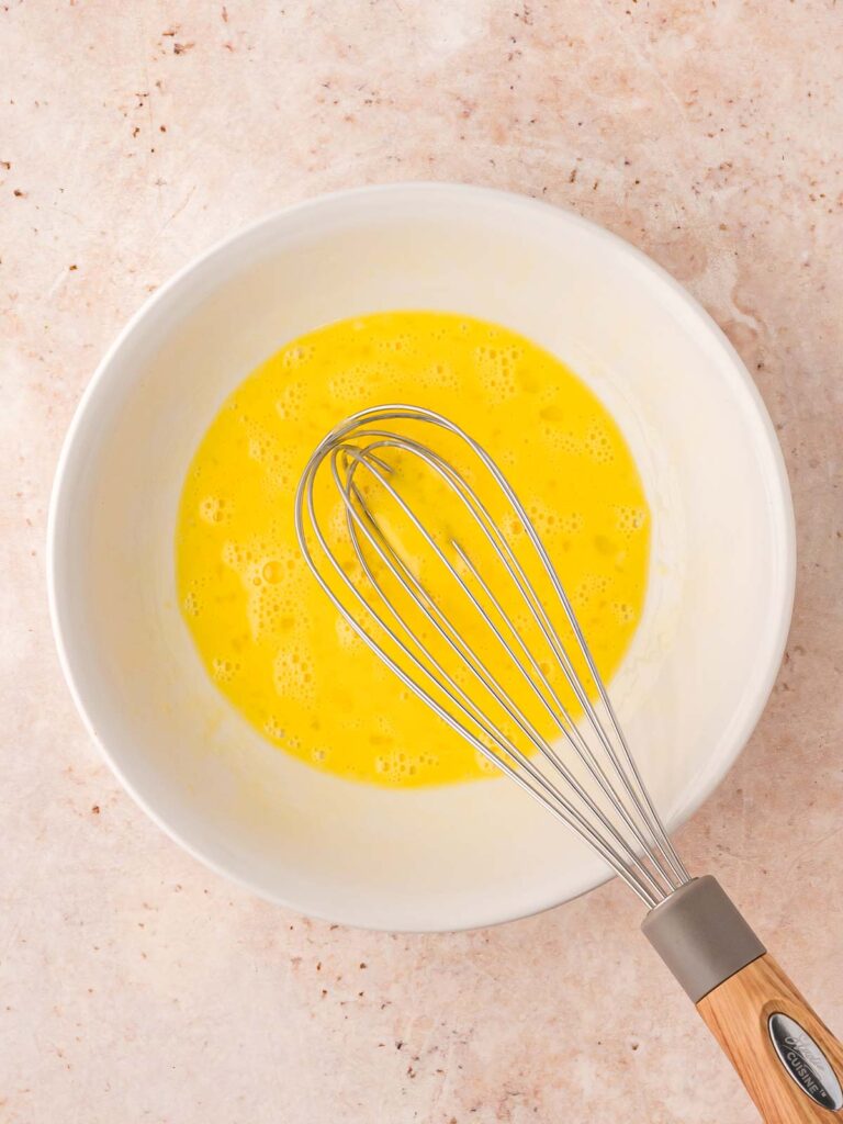 Egg wash in a bowl with a whisk.