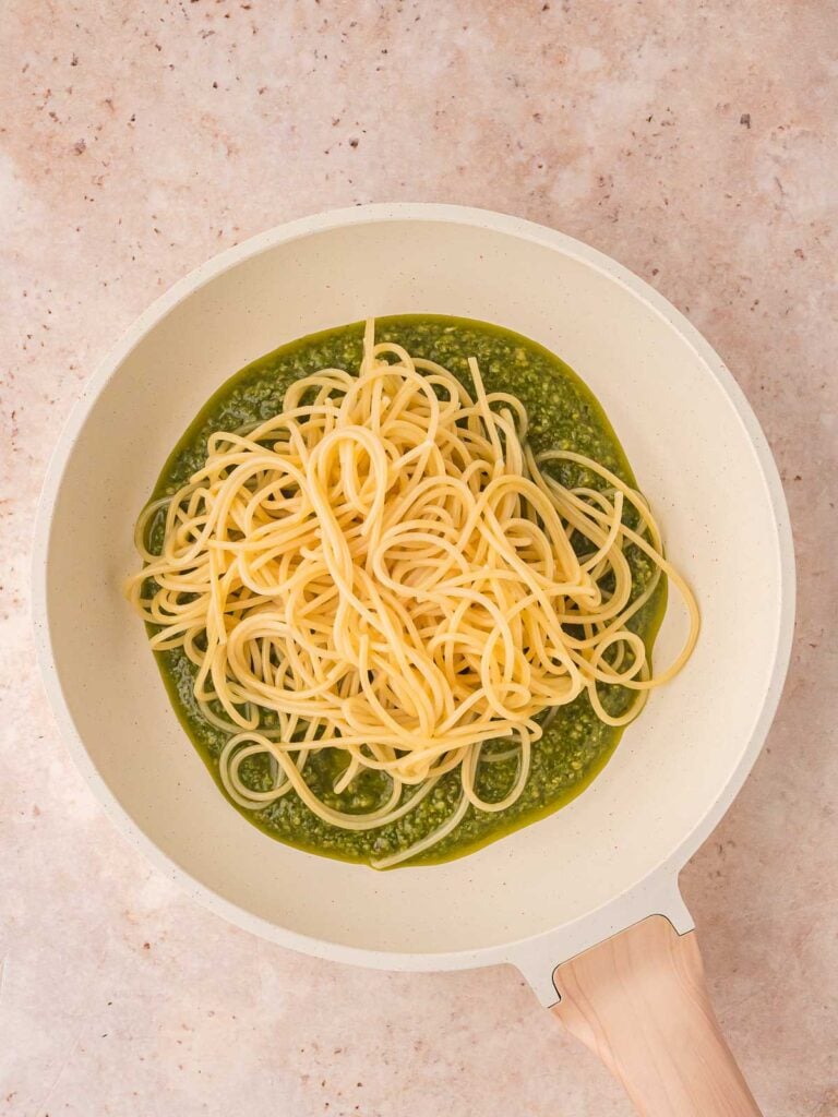 Spaghetti being added to the pesto in the pan.