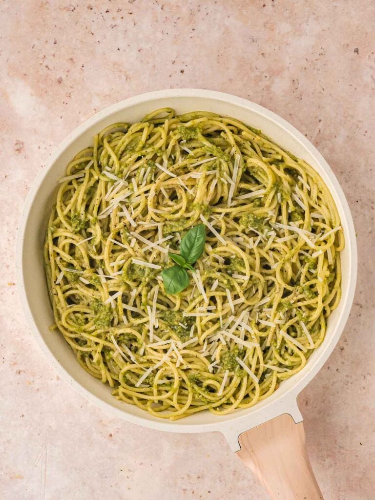 Spaghetti tossed with the esto in a pan with parmesan and basil added on top.