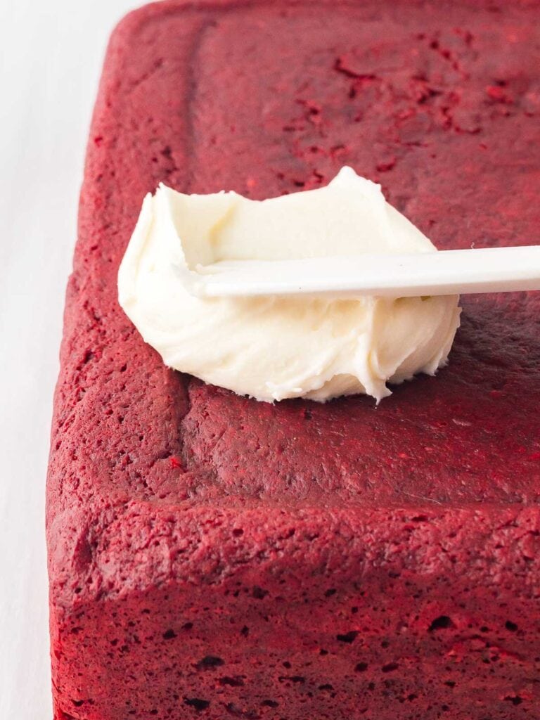 Cream cheese being spread onto the red velvet brownies.