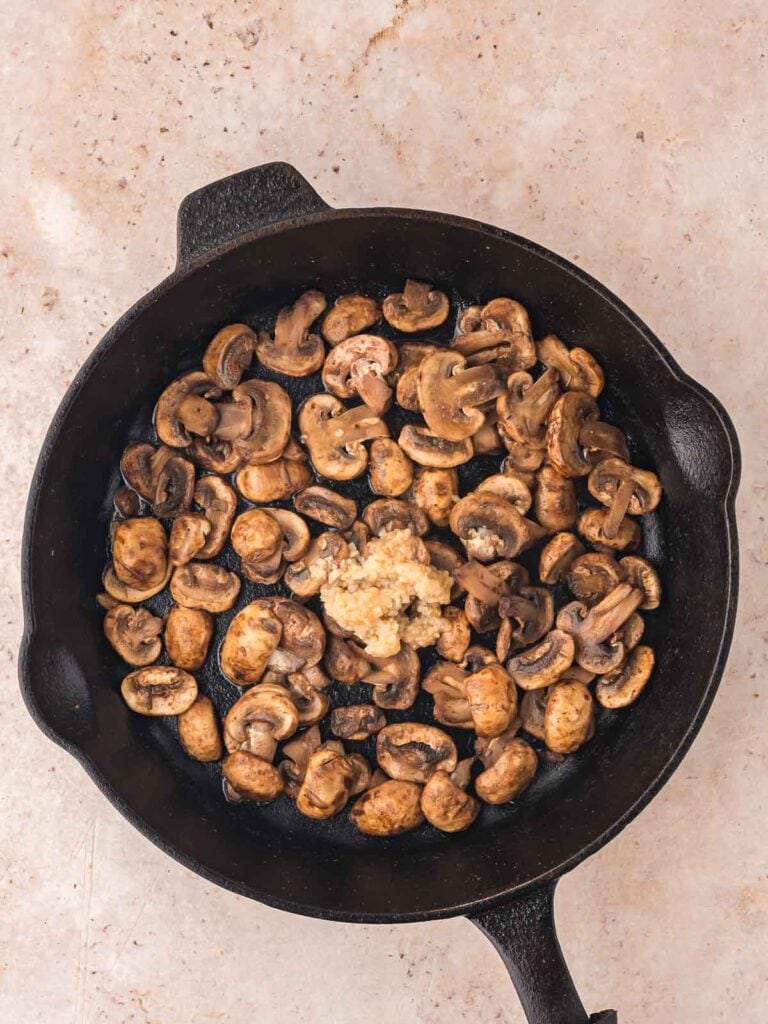 Mushrooms and garlic frying in a cast iron pan.