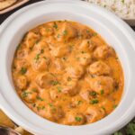 A white crock pot with Butter Chicken Meatballs inside.