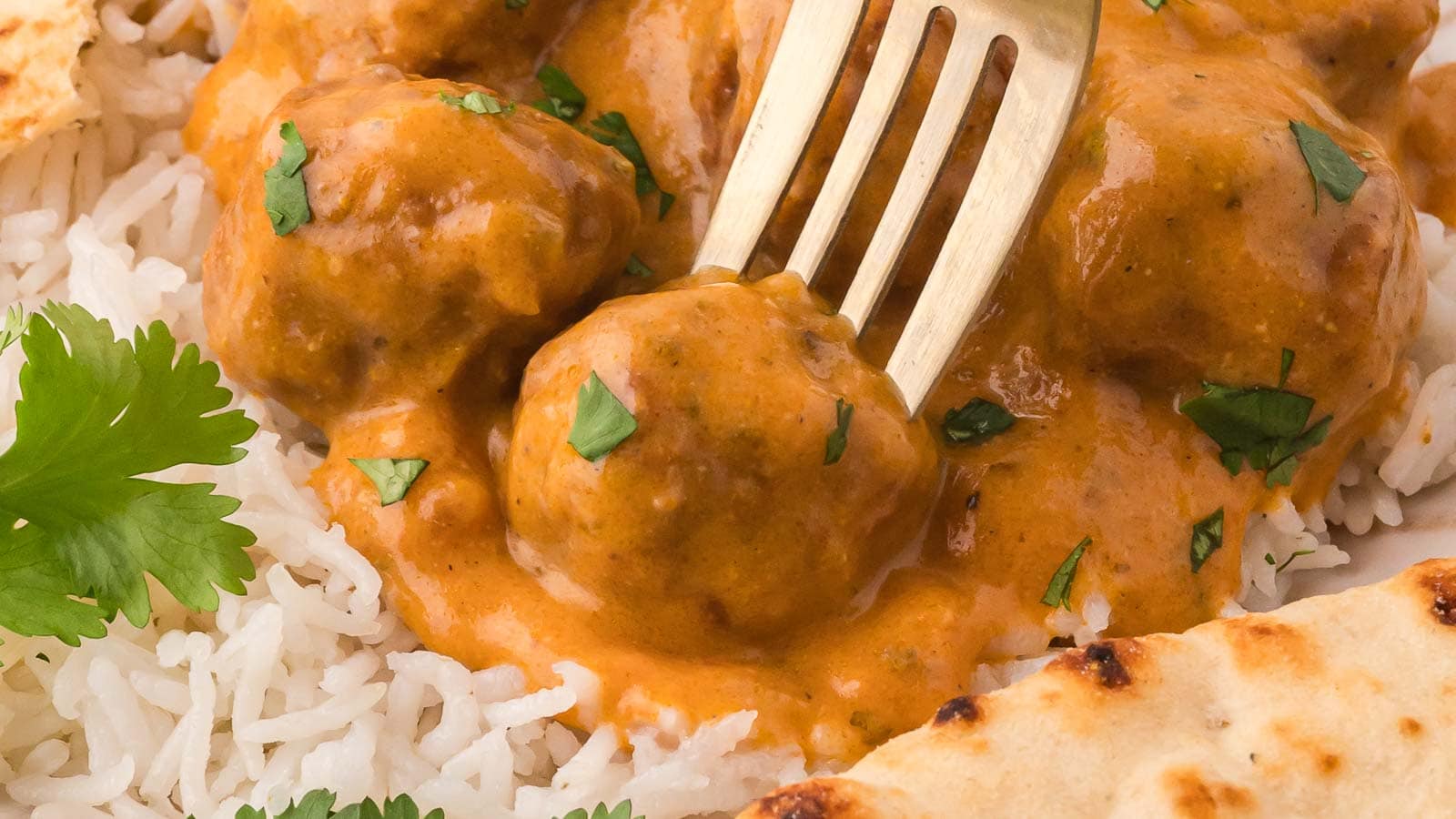 A gold fork in a butter chicken meatball on a plate with rice.