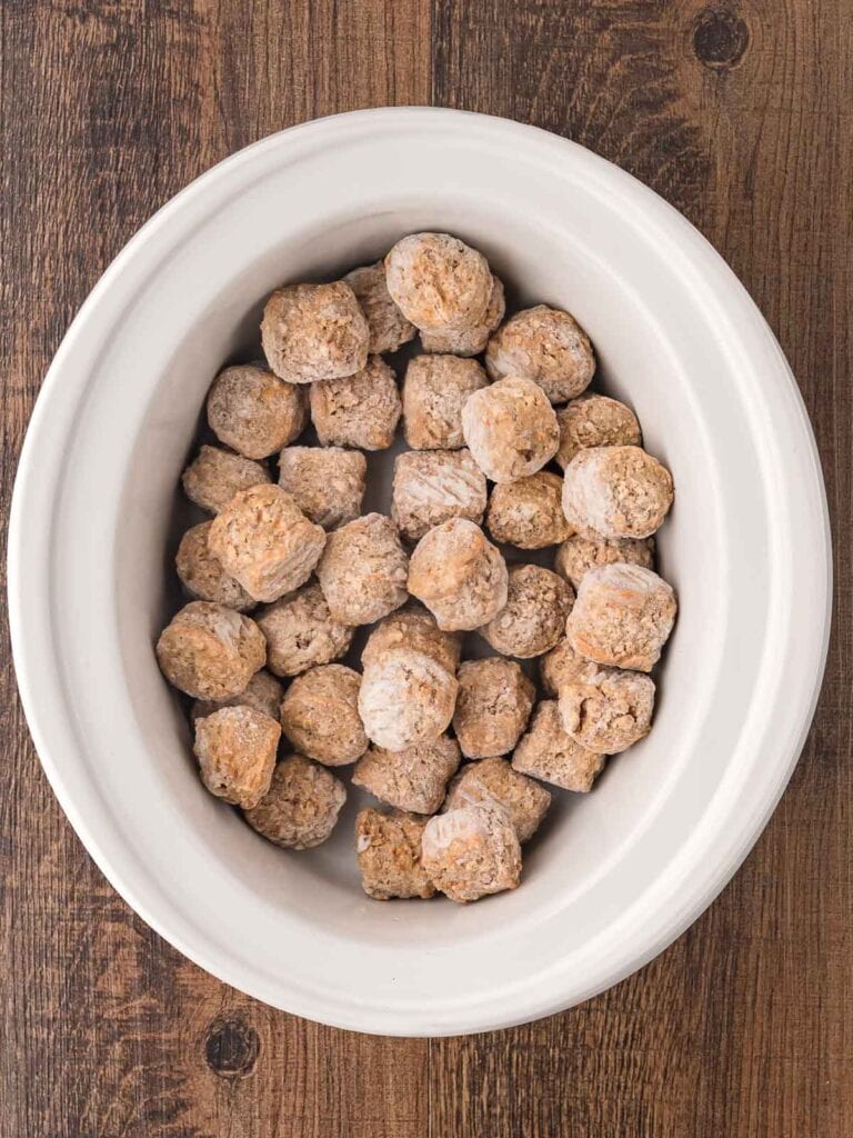 Frozen meatballs in a white slow cooker.