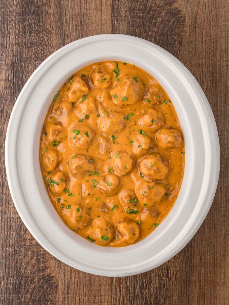 Cooked Slow Cooker Butter Chicken Meatballs in a white slow cooker.