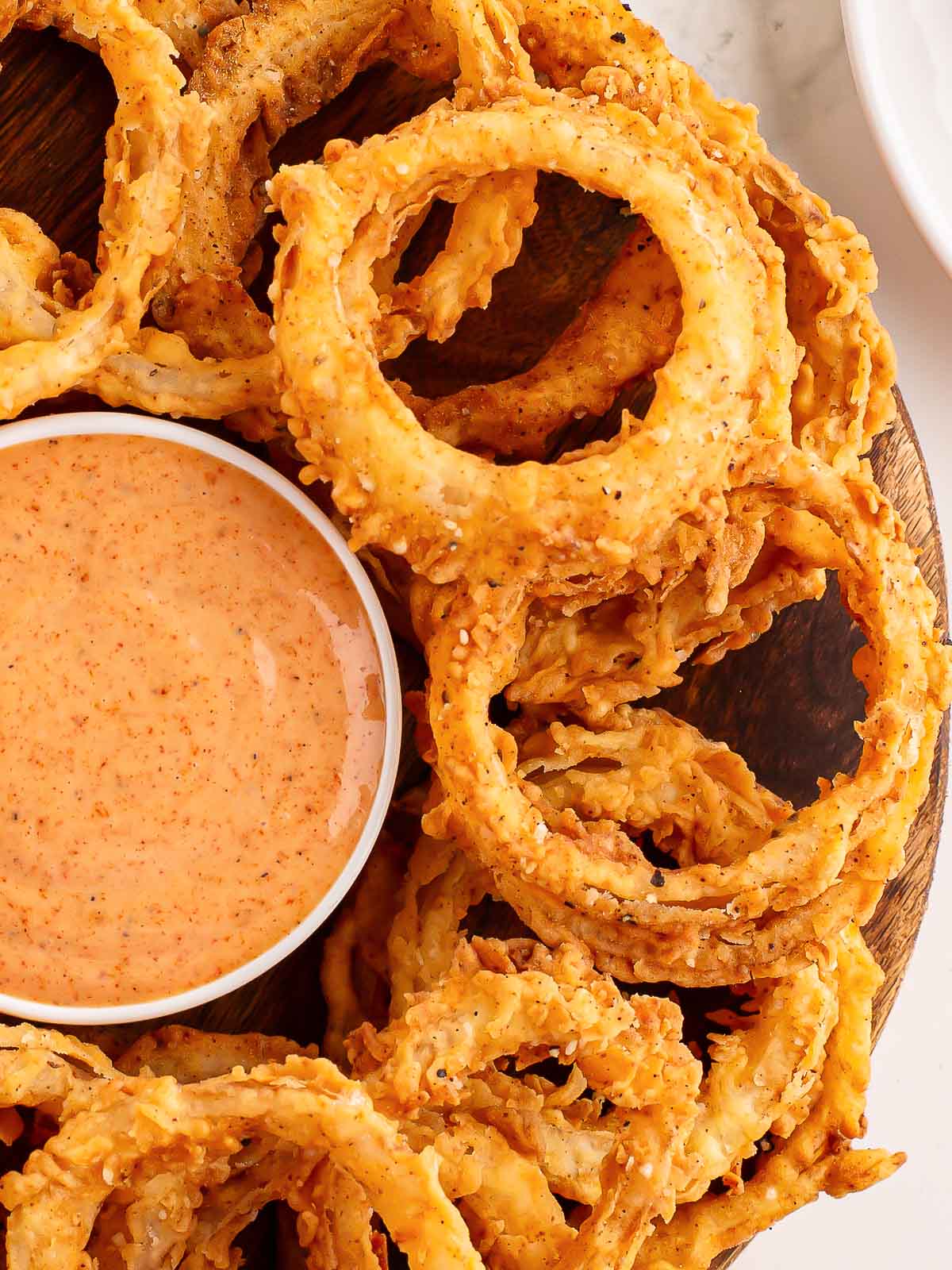 A plate full of Onion Rings with a bowl of sauce in the center.