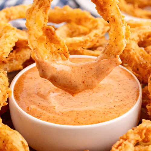 An Onion Ring being dipped into sauce.