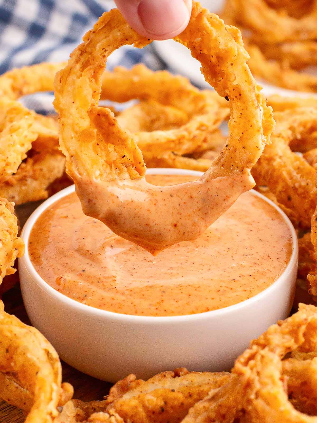 An Onion Ring being dipped into sauce.