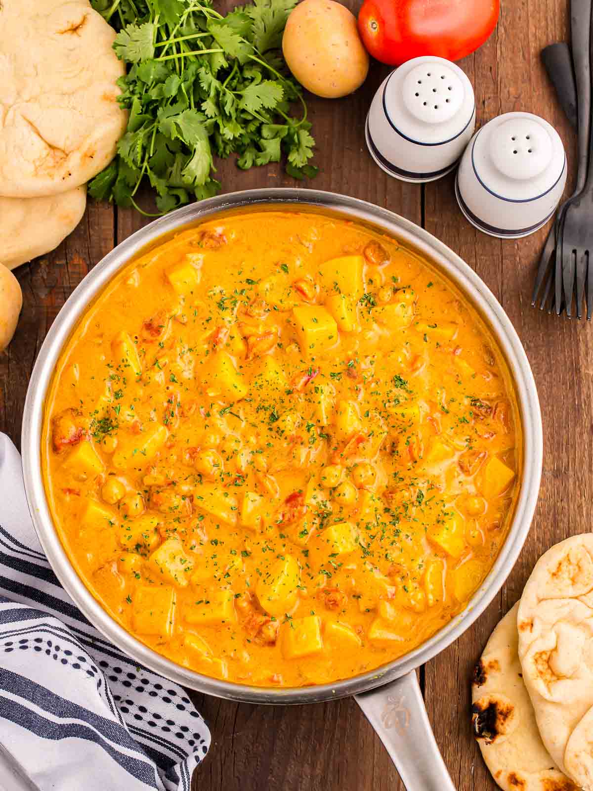 Overhead shot of Potato Curry in a pan on a dark wood table.