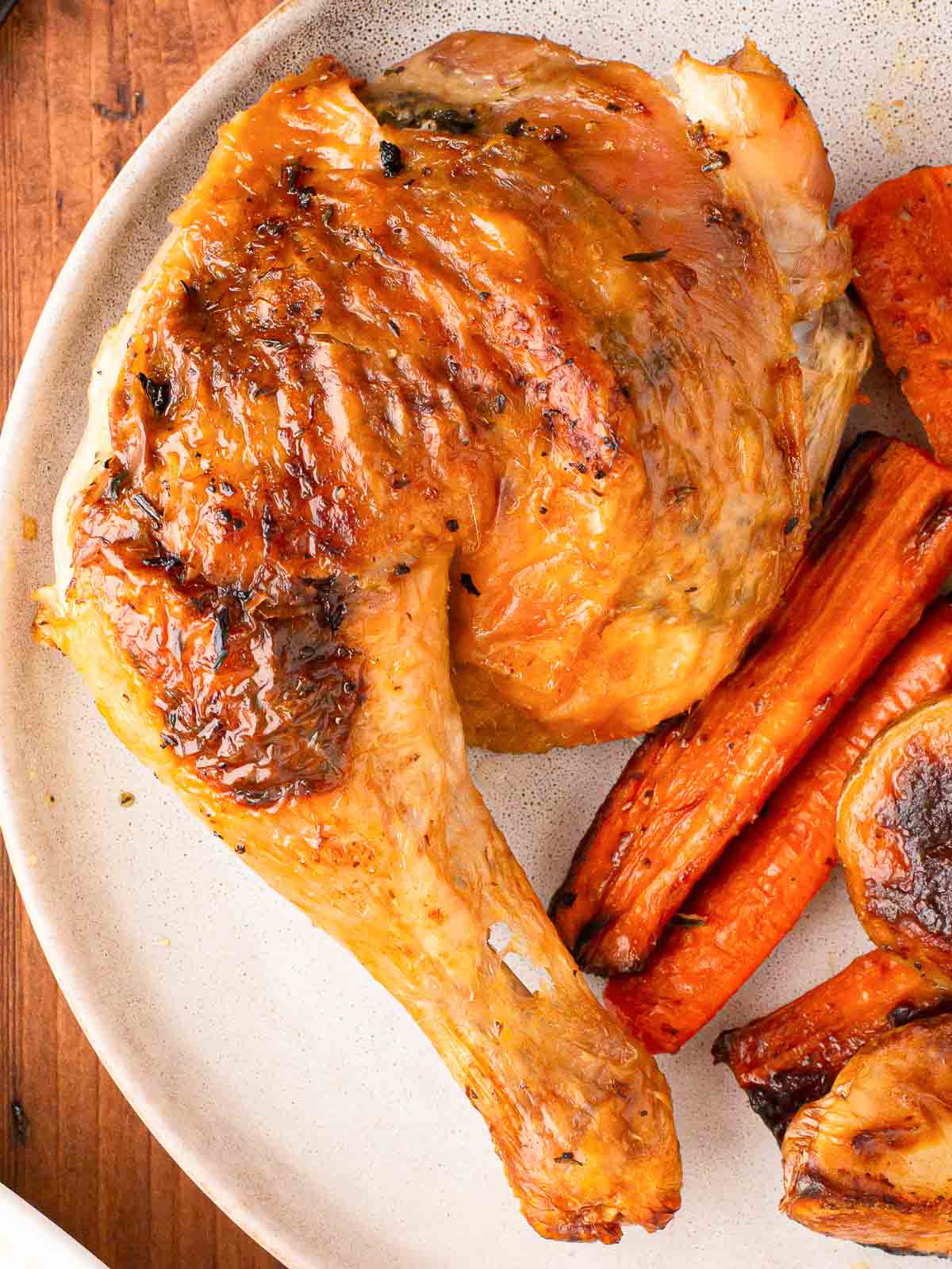 A roasted chicken leg on a plate with carrots.