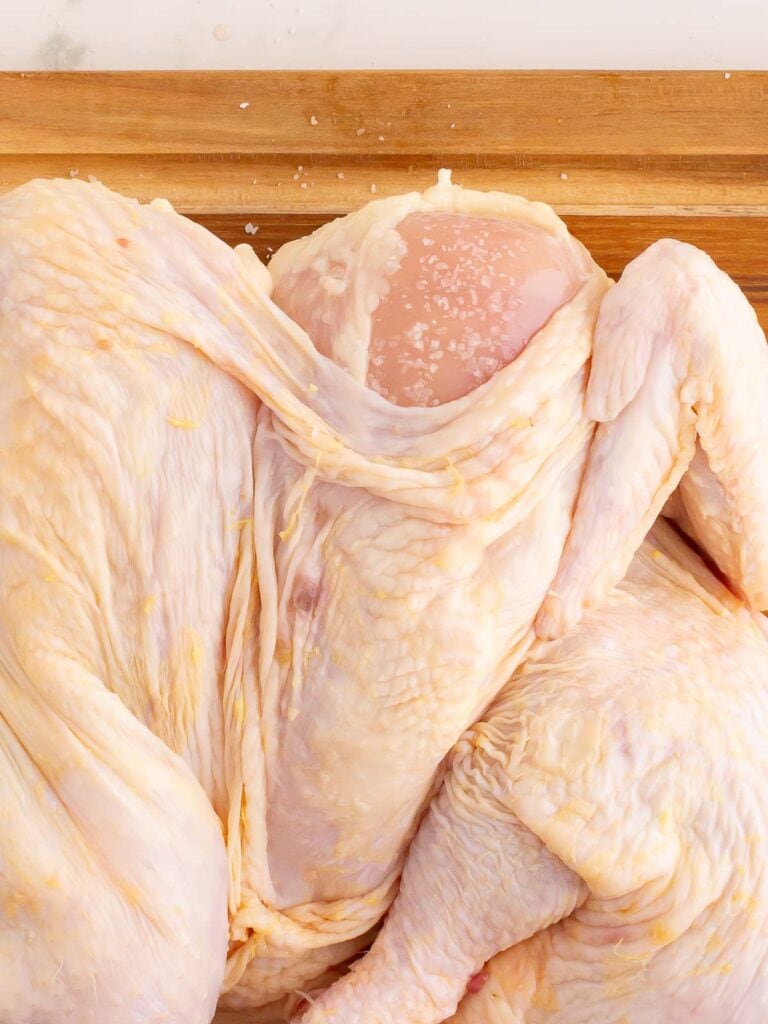 A raw chicken with the skin pulled back with salt on the meat.